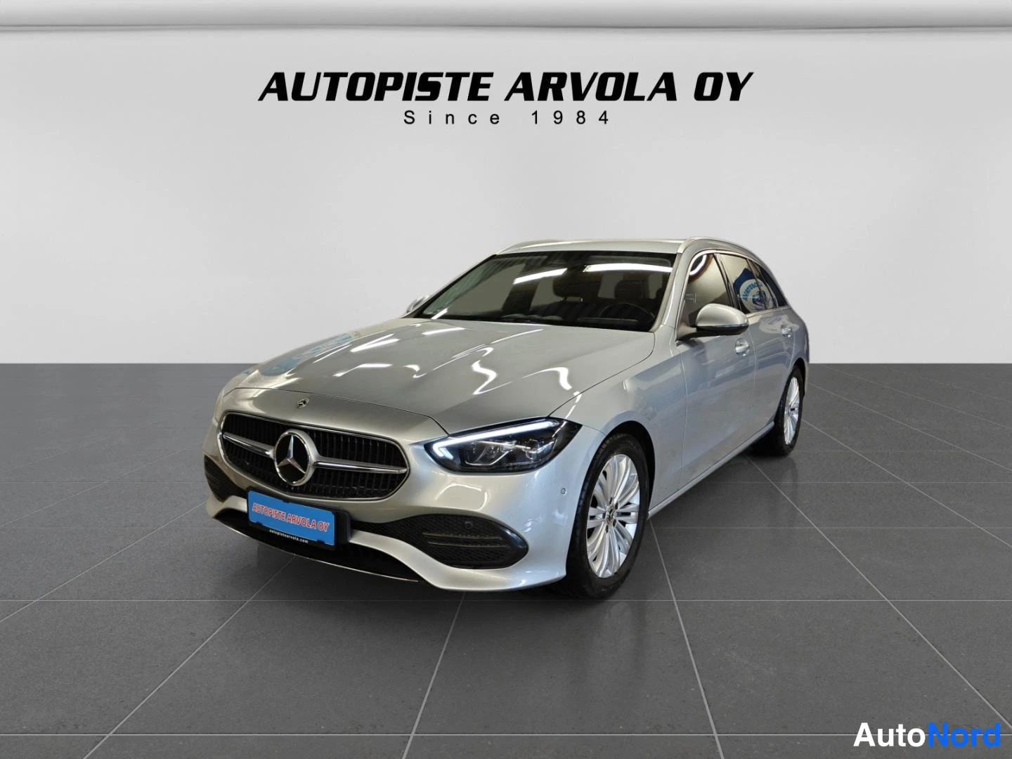 Etuviisto, nokka vasemmalle: Hopeanvärinen Mercedes-Benz farmariauto etukulmasta studiovaloisaan näyttelytilaan.
