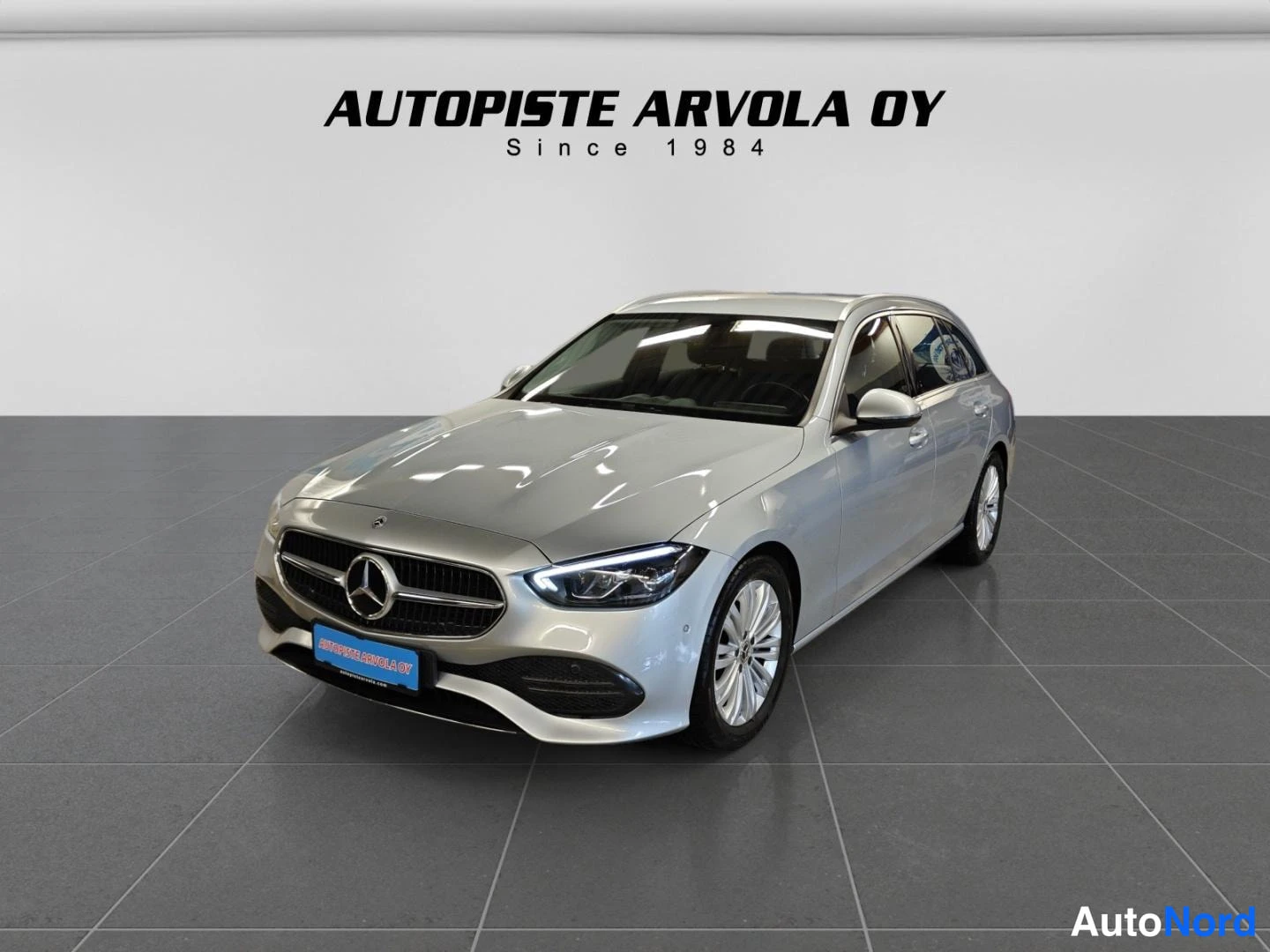 Etuviisto, nokka vasemmalle: Mercedes-Benz C-asema-auto etukulmasta, hopeinen kori studiohallissa