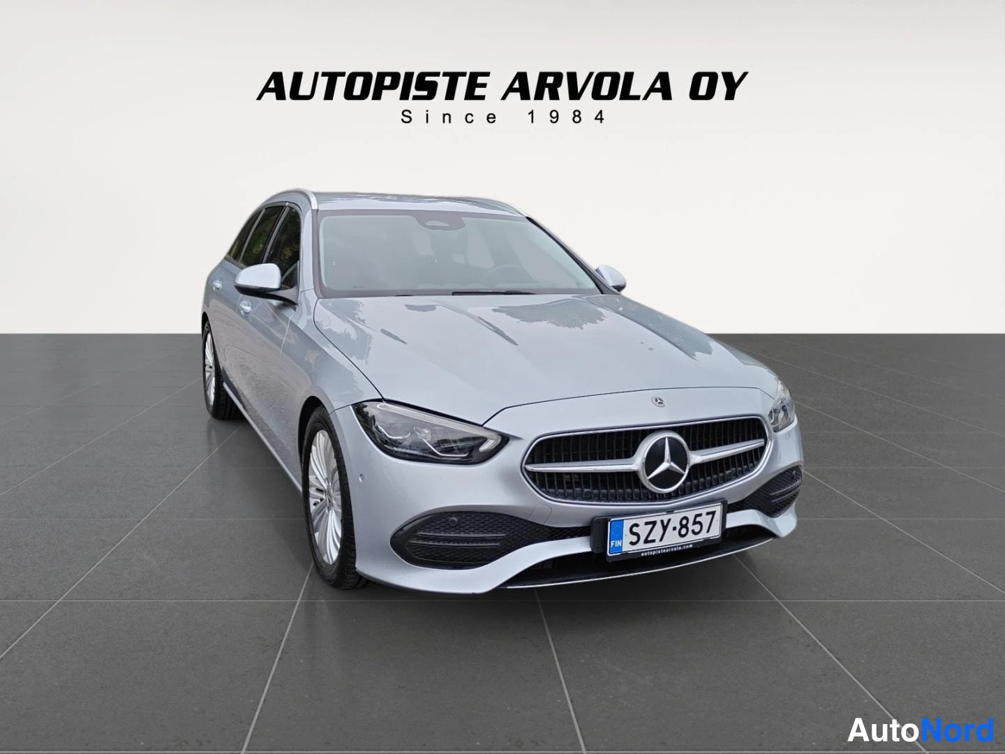 Etuviisto, nokka oikealle: Hopeanvärinen Mercedes-Benz C-mallin farmariauto suoraan edestä hieman sivusta kuvattuna, rekisteritunnus.