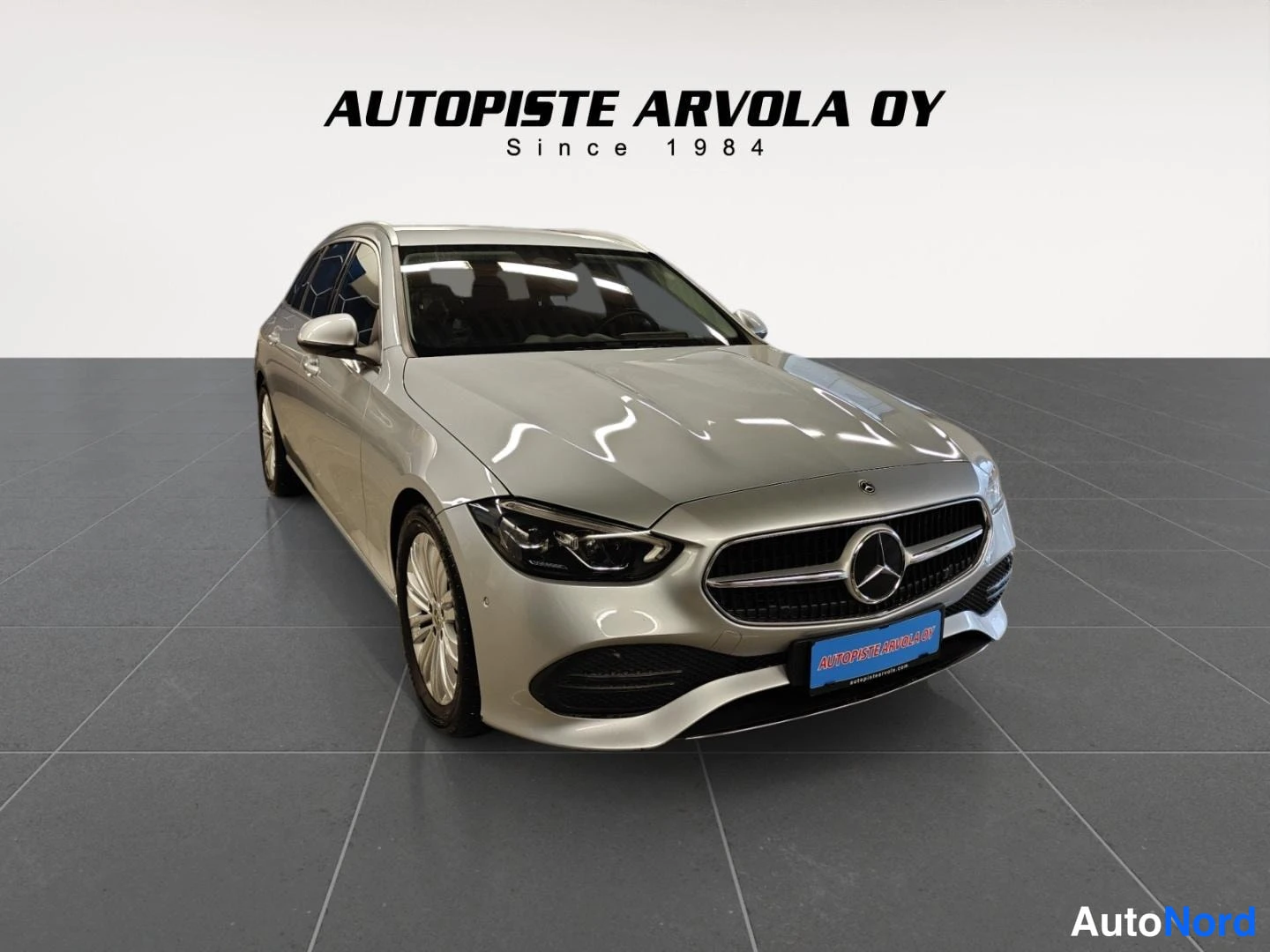 Etuviisto, nokka oikealle: Mercedes-Benz C -farmari, hopeanvärinen, edessä kolmannelta kulmalta, nokka oikealla.