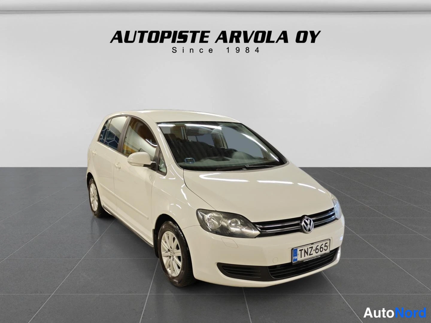 Etuviisto, nokka oikealle: Valkoinen Volkswagen Golf Plus -henkilöauto etuviistosta sisätiloissa, rekisteritunnus.