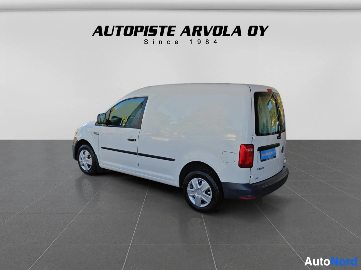 Takaviisto: Valkoinen Volkswagen Caddy -pakettiauto takaviistosta kuvattuna, yhdet takana olevat sivuovet ja tummat puskurit.