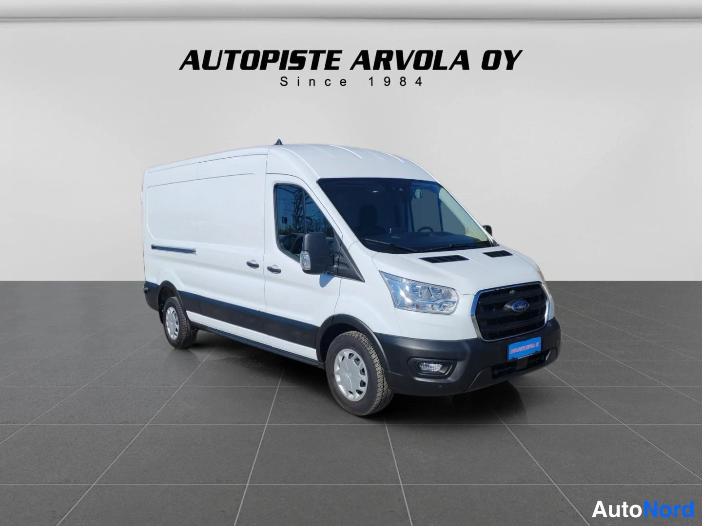 Etuviisto, nokka oikealle: Ford Transit -pakettiauto edessä oikealta valokuvattuna, valkoinen korimusta pesu- ja servaalussa.