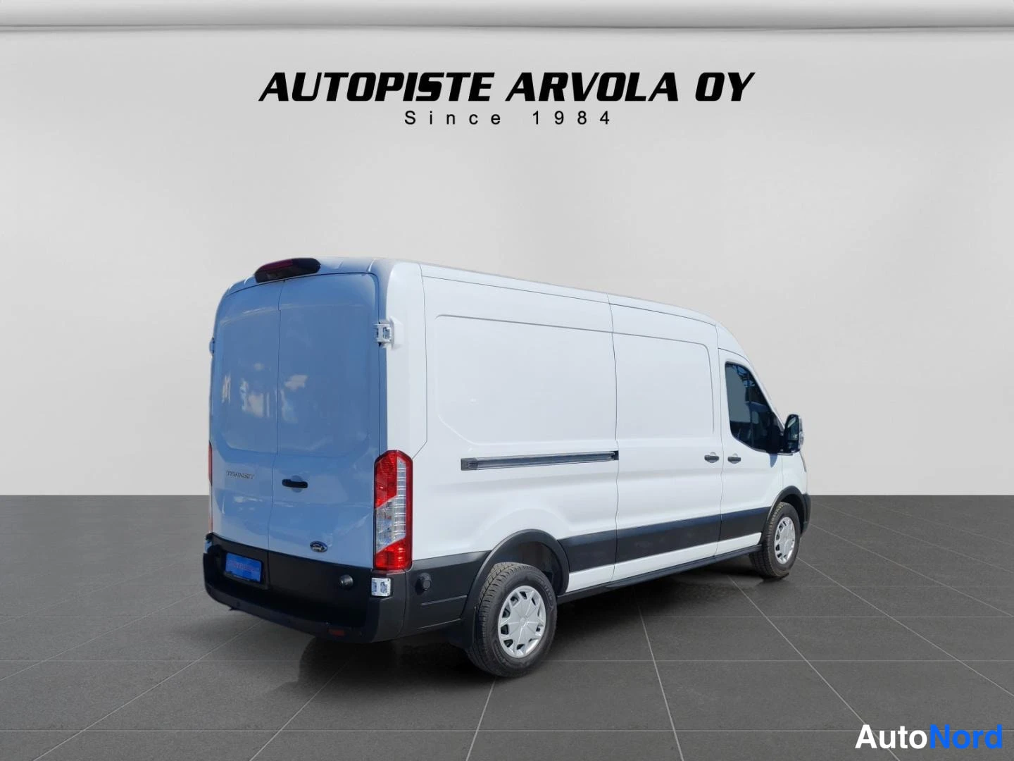 Takaviisto: Valkoinen Ford Transit -pakettiauto takaa kolmannenvälinen kuvakulma, takaovet ja sivuseinä näkyvät, Autopiste Arvola Oy -studiovaalea tausta.