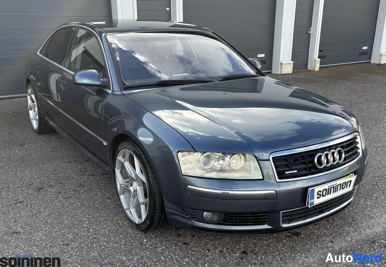 Etuviisto, nokka oikealle: Tummanharmaa sedan takakulmasta kuvattuna, keulakulta ja Audi-merkki näkyvät.