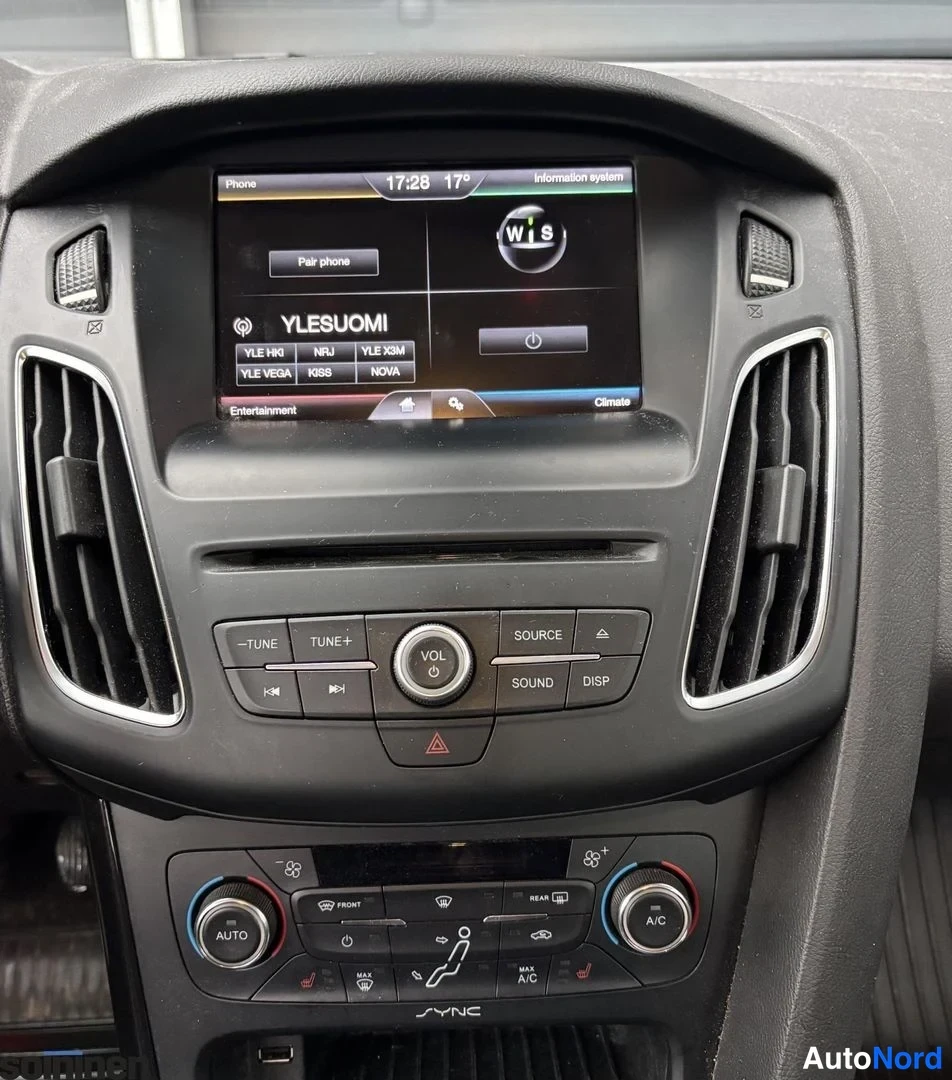 Yksityiskohta: Kojetaulun keskikonsoli: Ford SYNC-näyttö, radiolähettien YLESUOMI-valinta, ympyränappeja ja ääniohjaimia, alapuolella kaksialueinen ilmastointipaneeli AUTO- ja