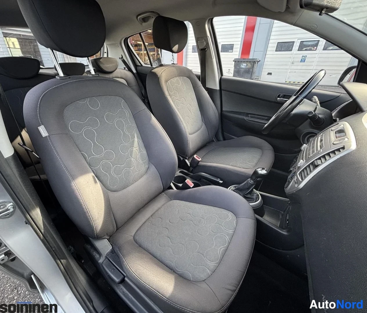 Takaviisto: Näkymä Hyundai i20:n etumatkustajan penkiltä ohjaamoon; kaksi tummaa kuviollista etuistuinta, ohjauspyörä ja keskikonsoli näkyvät.