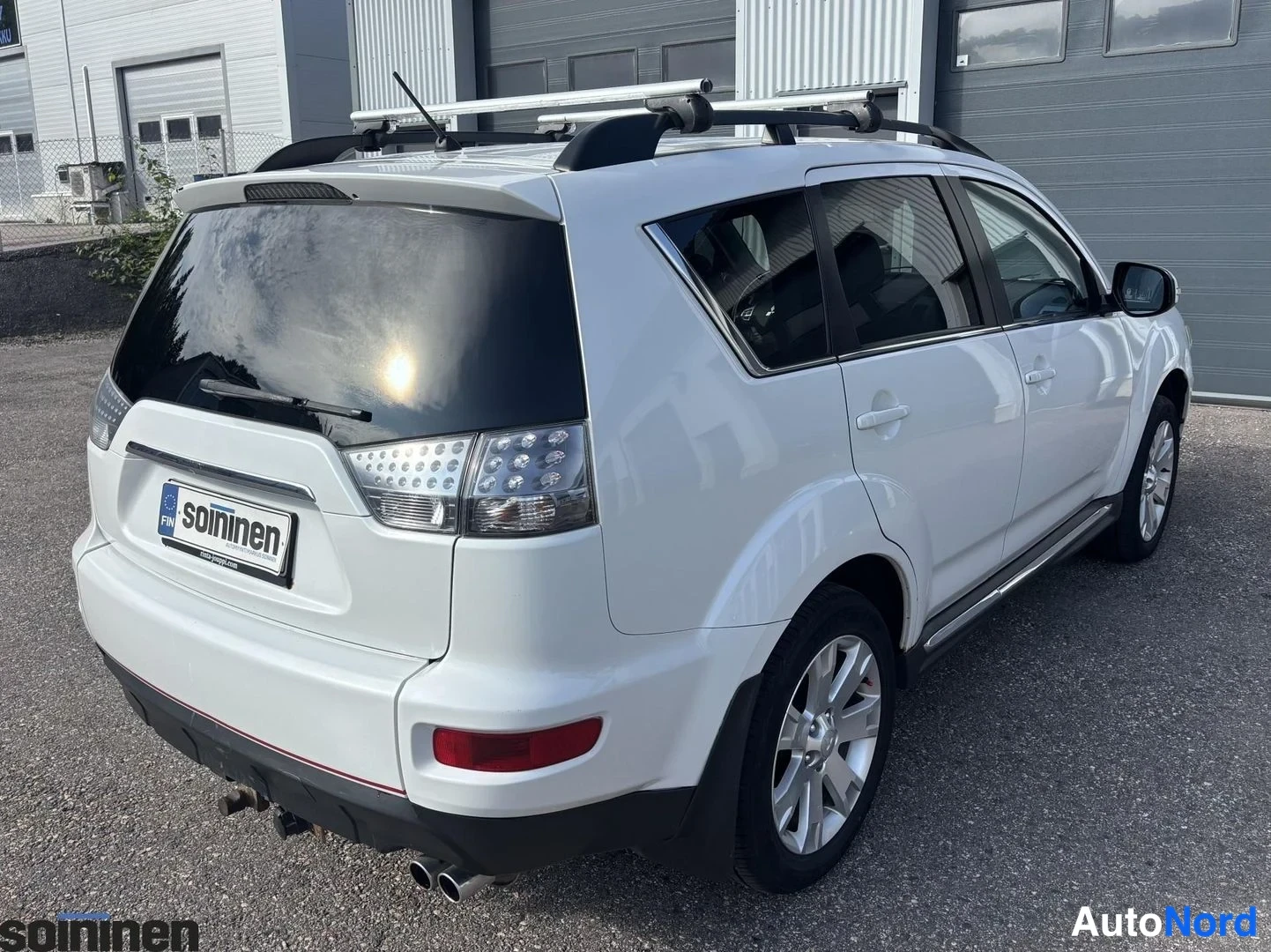 Takaviisto: Mitsubishi Outlander -maasturin takapää ja oikea kylki kuvattu takakulmasta, kattotelineet, saitit ja kaksoispakoputki näkyvät.