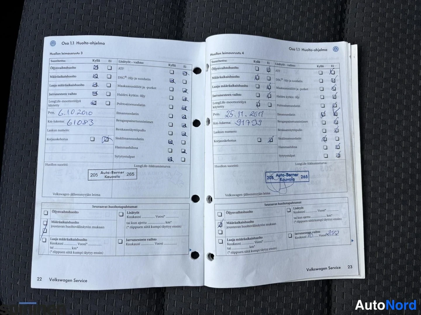 Yksityiskohta: Avoin Volkswagen-huoltokirja, sivut 22-23, huoltojen merkinnät 6.10.2010 (61 083 km) ja 25.11.2011 (91 439 km), Auto-Berner Kouvolan leimat.