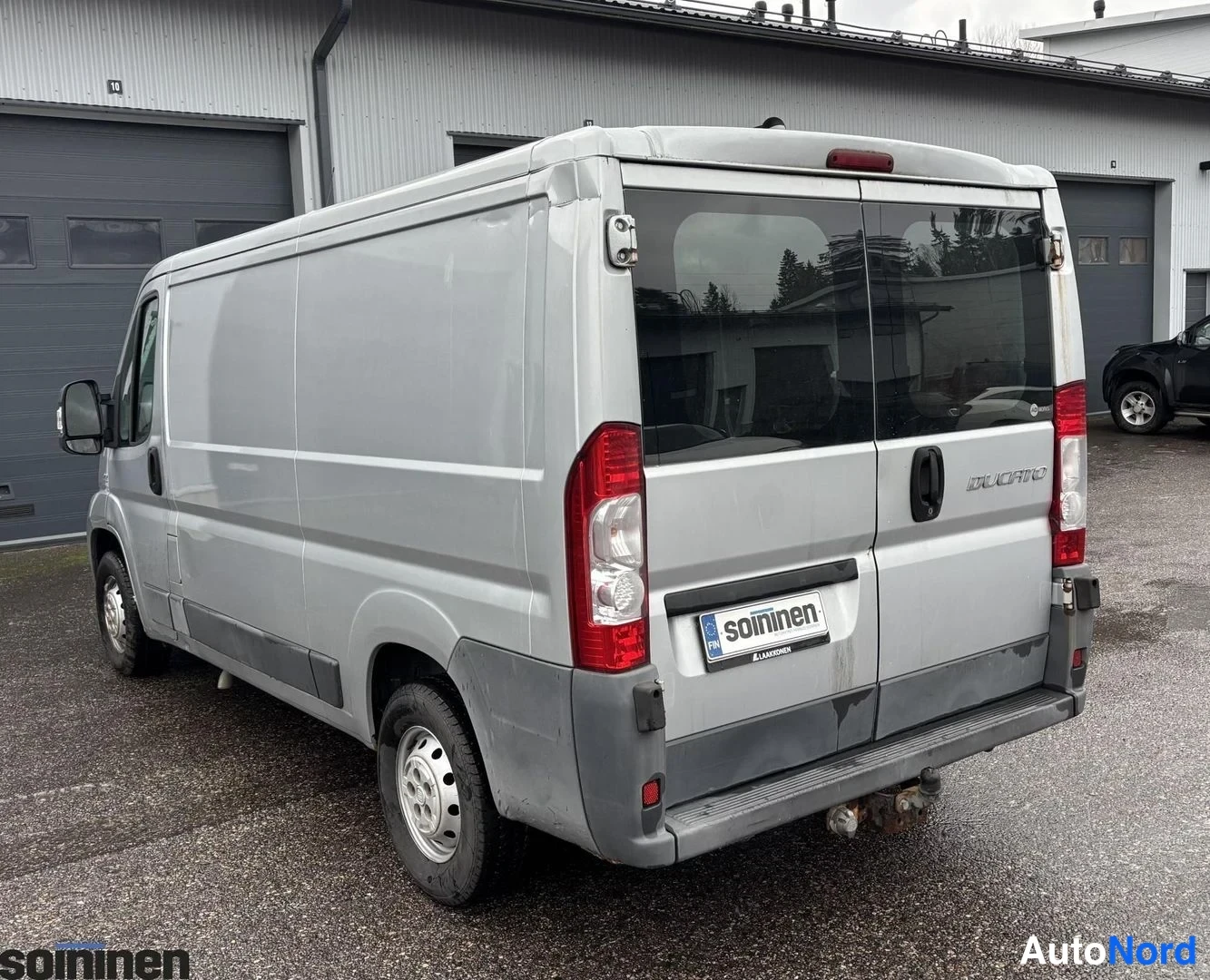 Takaviisto: Rear three-quarter of silver Ducato van. Vertical red tail lights visible on both sides. Rear doors have no glass in cargo area. Hitch receiver installed below