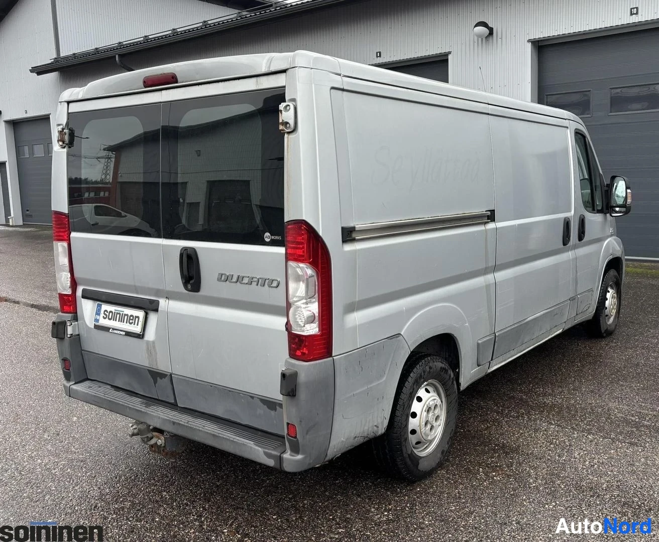 Takaviisto: Rear three-quarter of silver Ducato van showing rear doors and full length of driver's side. Faded watermark-like text on side panel reads 'Se yllättää'. Cargo