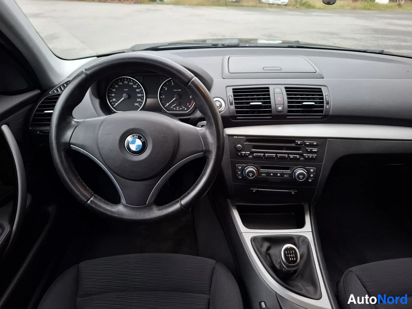 Muu: Näkymä tuulilasista kojelautaan: BMW-ohjauspyörä, mittaristo ja keskikonsolin radiolaite.