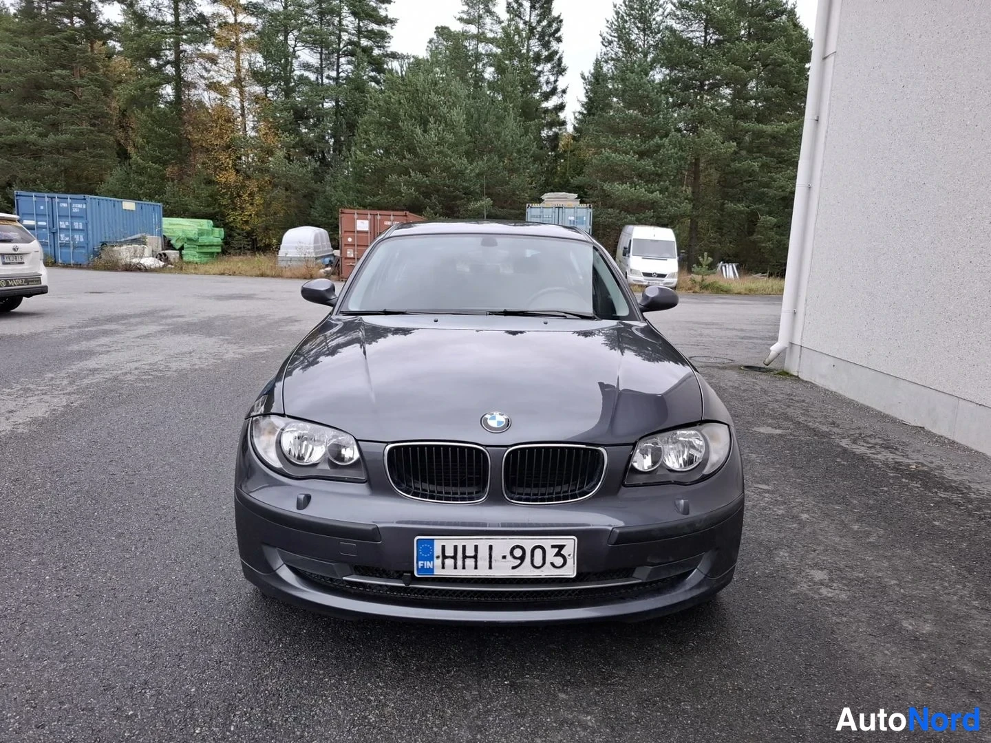 Edestä: Auton etuselkäkymä: tummanharmaa BMW, rekisteritunnus HHl-903, edessä pysäköityneenä pihamaalla.