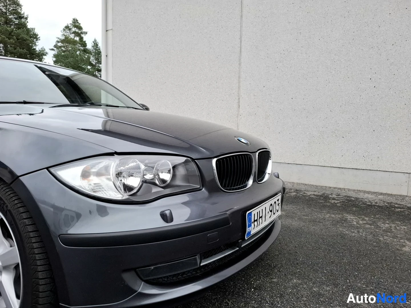 Etuviisto, nokka oikealle: Sivusta-etuvinkkelistä kuvattu tummanharmaan BMW:n keula: etumoottoritila ja etupyörän yläosa näkyvät, rekisteritunnus HHl-903.