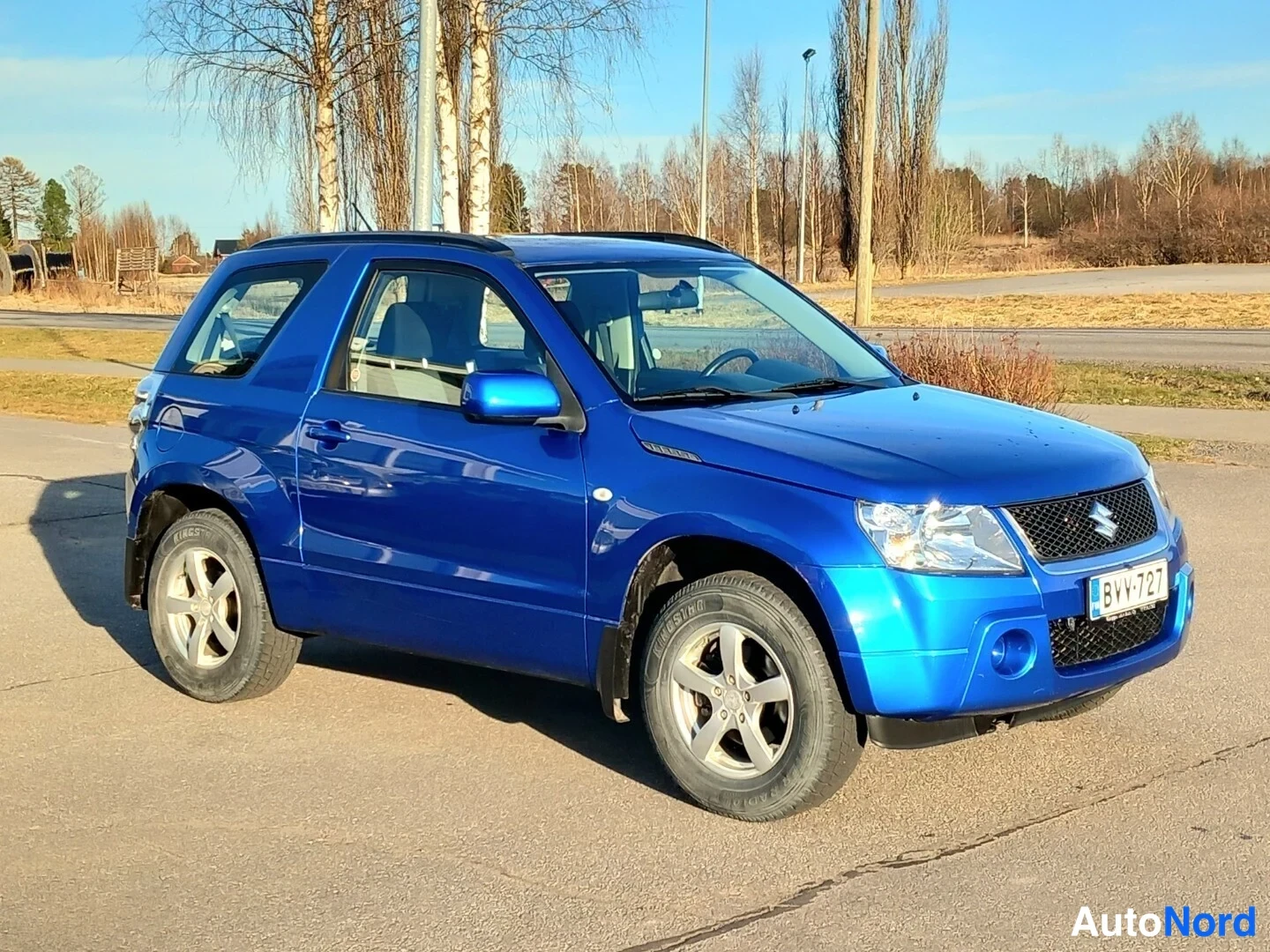 Etuviisto, nokka oikealle: Sininen kolmiovinen Suzuki Grand Vitara kolmasosaedestä, keula oikealla, rekisterikilpi.