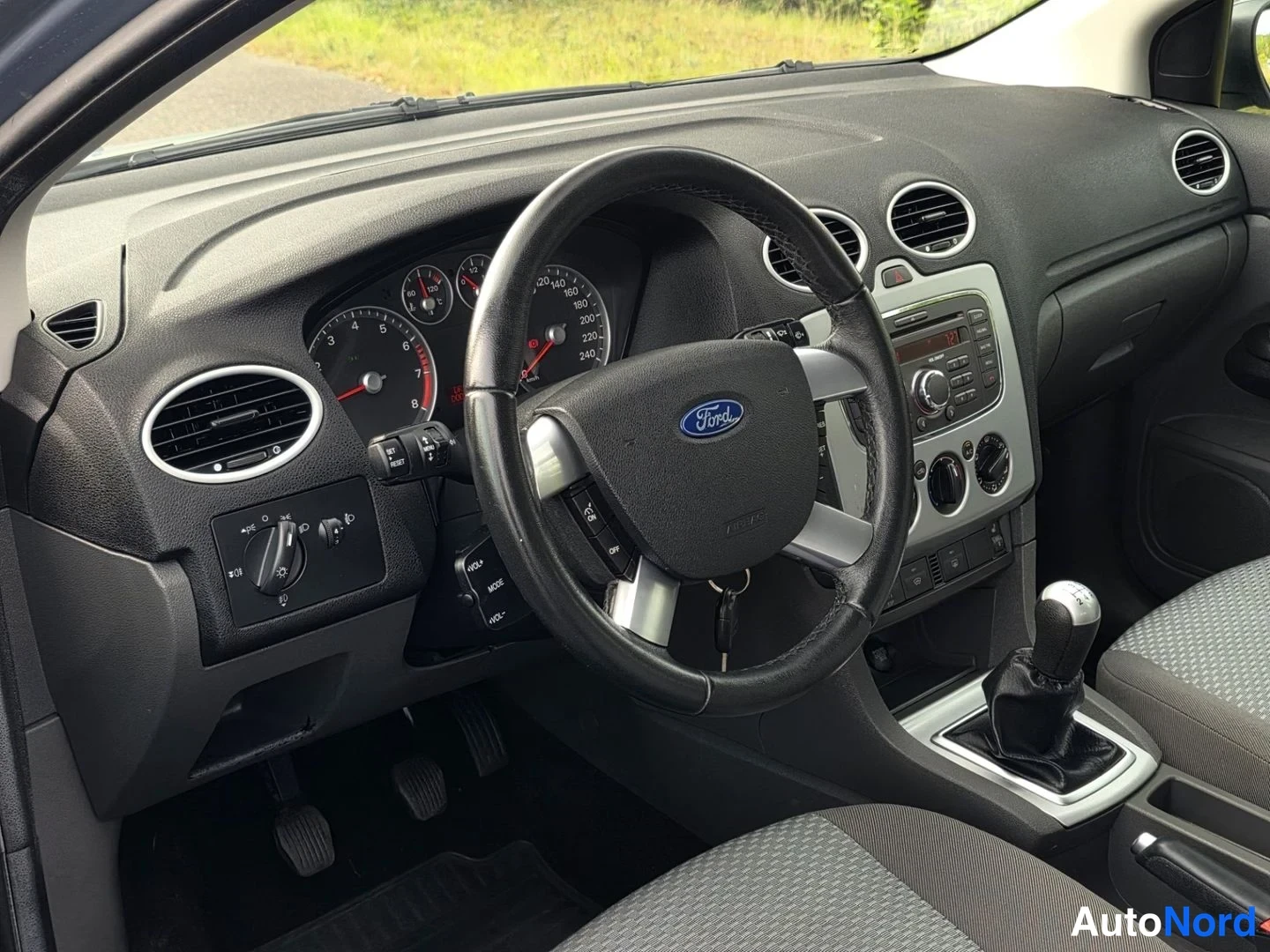 Asiakirja: Ford Focusin ohjaamosta viistosti: ohjauspyörä, mittaristo, keskikonsolin radio ja manuaalivaihteen vipu.