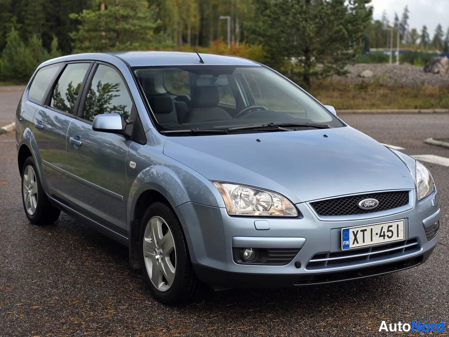 Etuviisto, nokka oikealle: Ford Focus -farmari etualalta oikealta, harmaansininen kori, etumoottoritilan etusarvi ja Ford-merkki näkyvät, rekisterikilpi.