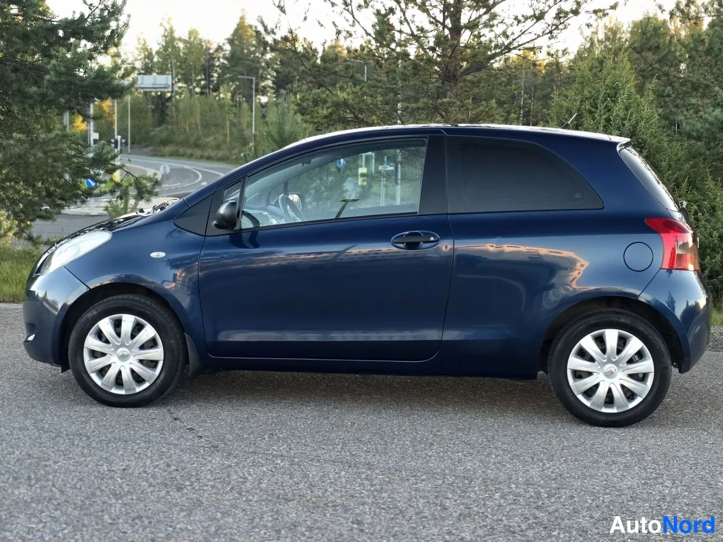 Sivulta: Tummansinisen Toyota Yaris -viistoperän sivukuva; kaksi ovea, säästönäyttöä muistuttava hopeavannehelpotus ja takavalojen reuna erottuvat.