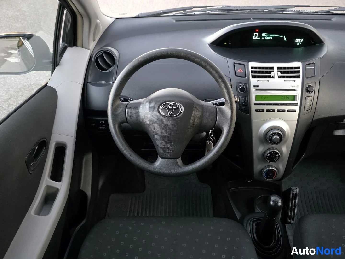 Muu: Kuljettajan näkemys Toyota Yariksen ohjaamoon: ohjauspyörä, mittaristo ja radio.