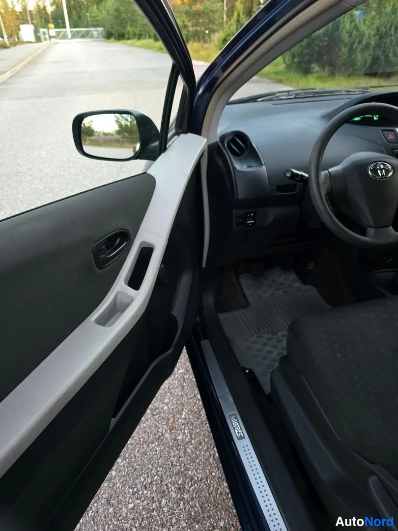 Muu: Avattu kuljettajan ovi Toyota Yariksessa: oven sisäpaneeli, sivupeili ja olokynkäs nojailupaikka.