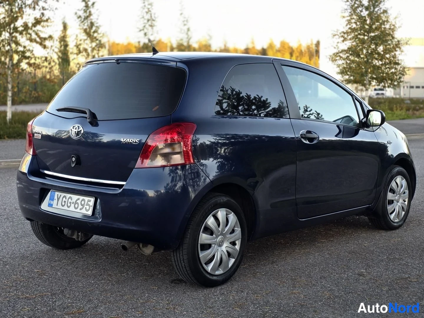 Takaviisto: Toyota Yaris -pieniauton takakulmanäyttö: tummansininen kolmiovinen auto, takavalot, -rekisterikilpi ja Toyota-merkki näkyvät.