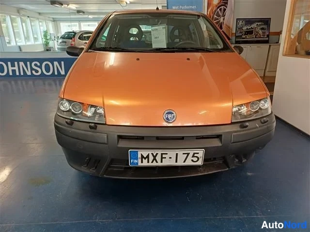Edestä: Oranssi Fiat etupaalta kuvattuna sisätilassa, rekisterikilpi.