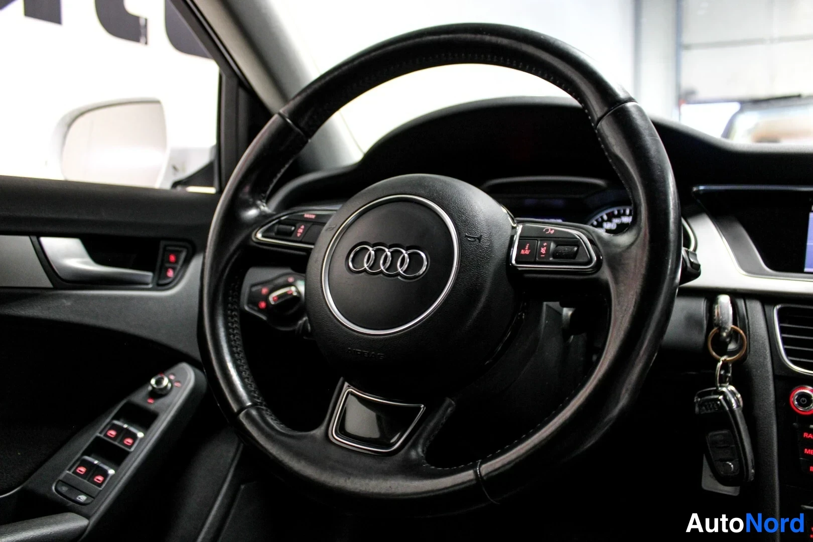 Edestä: Lähikuva ohjauspyörästä Audi-emblemillä, taustalla sähköikkunakytkimet ja avaimet lukurungossa.