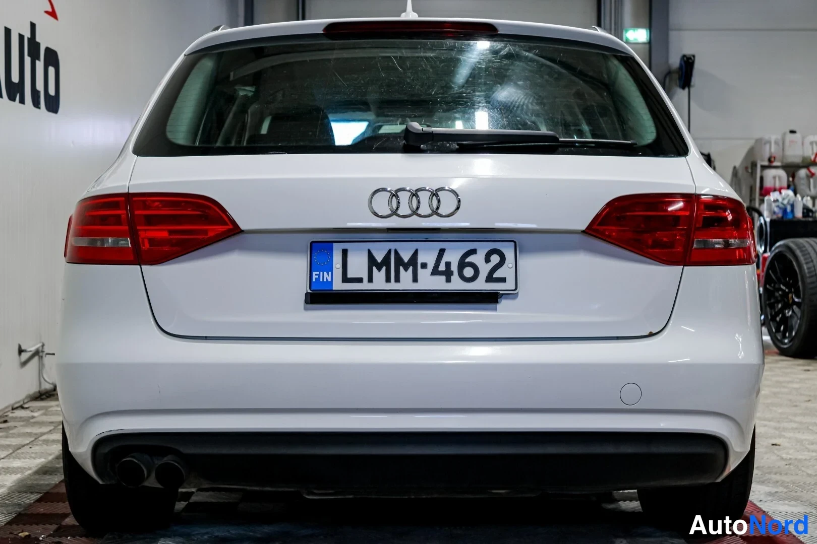Takaa: Auton takapää suoraan takaa: valkoinen Audi, punaiset takavalot, neljä renkaan rengasmerkkiä, kaksiosainen pakoputken suuh, rekisterikilpi FIN.