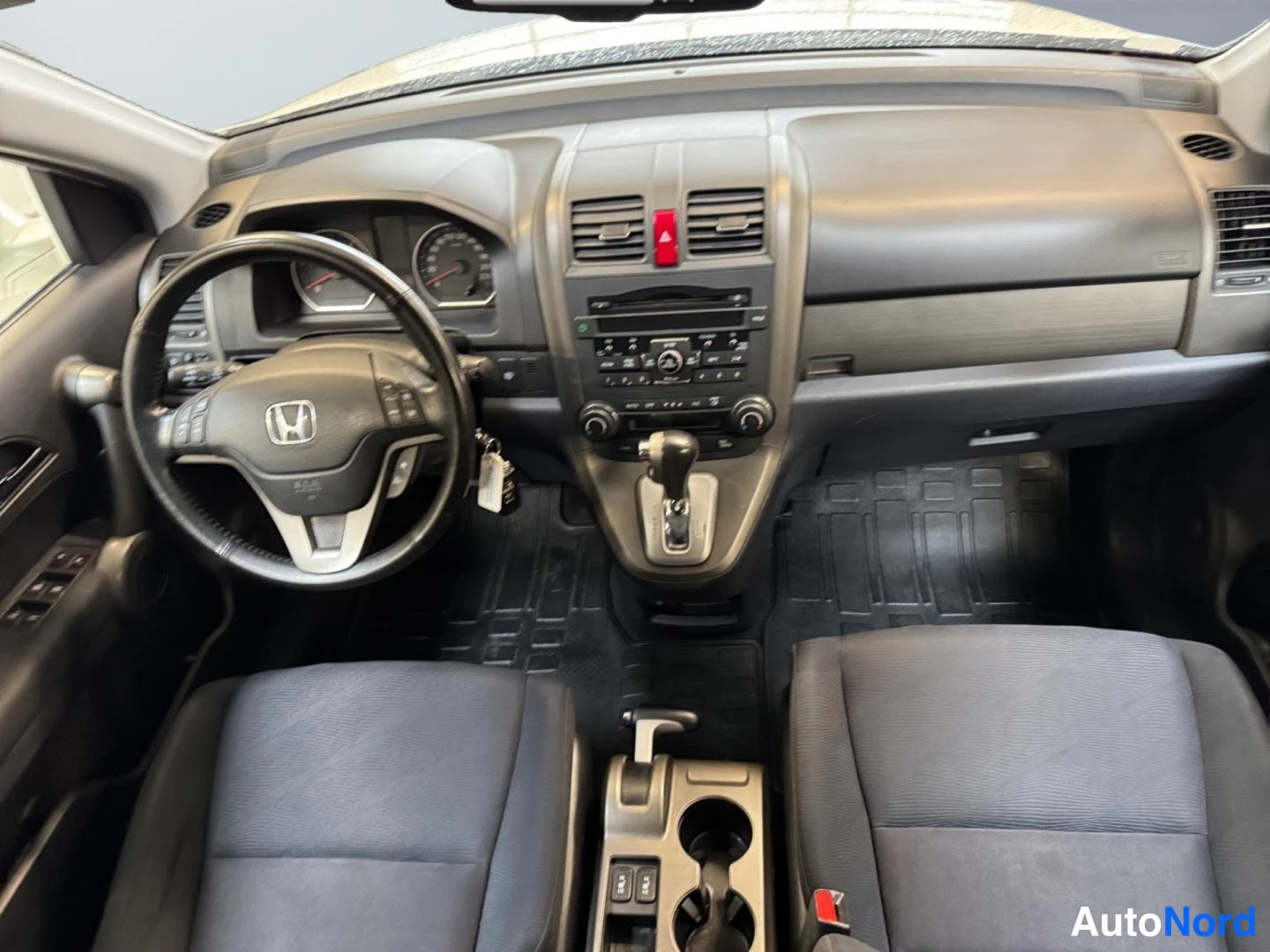 Muu: Honda CR-V:n kojelauta ohjaamosta kuvattuna: Honda-merkkinen ohjauspyörä, mittaristo, vaihtokahva ja automaattivalitsin.