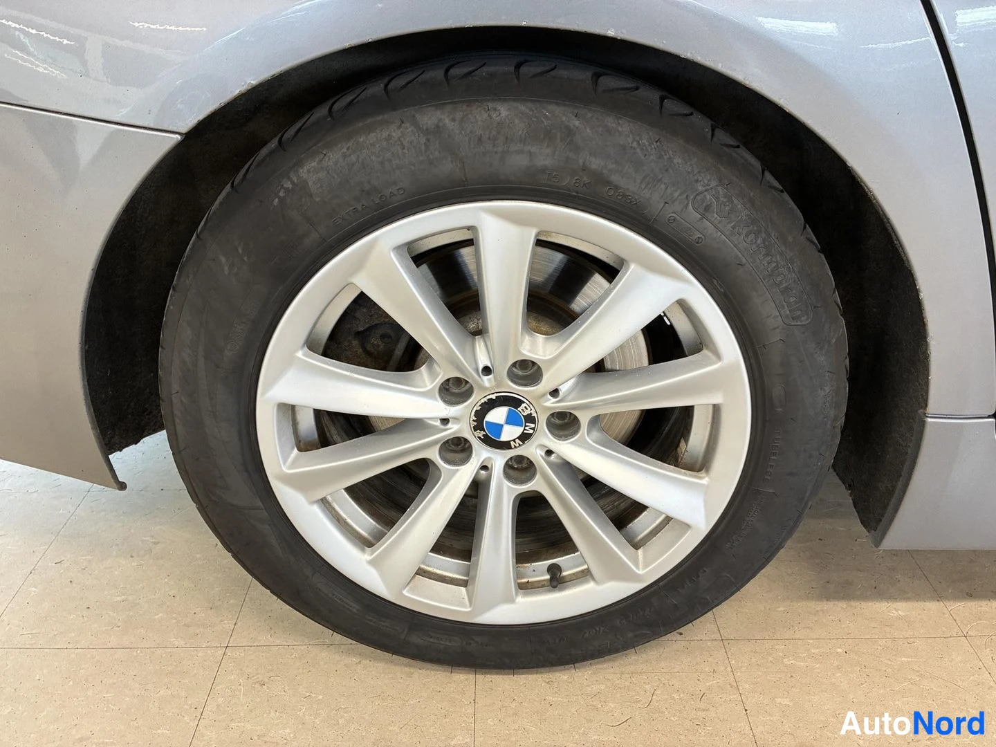 Sivulta: Lähipölykäs kuva auton pyörästä hopeanvärisellä vanteella ja BMW-merkillä.