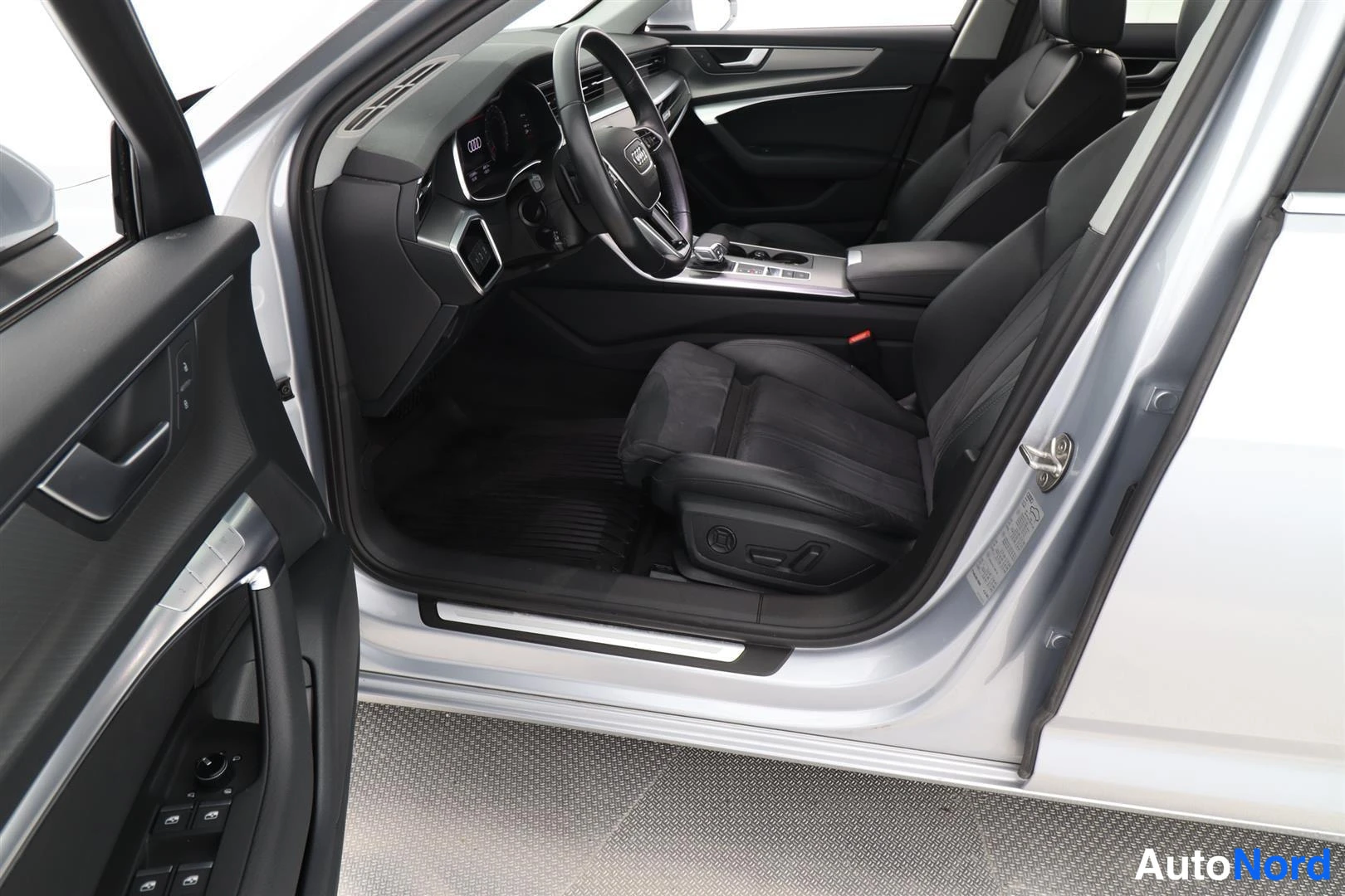 Muu: Audi A6:n ohjaamo nakyy avoimesta etiovesta: tummat istuimet, Audi-ohjauspyora ja keskitunneli