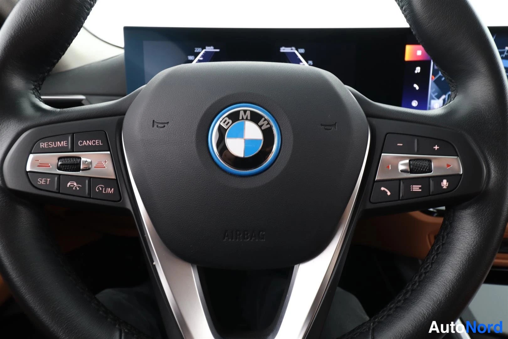 Ohjaamo: Direct close-up of a black three-spoke multifunction steering wheel with silver trim accents. The center features the BMW logo (blue and white roundel) surround