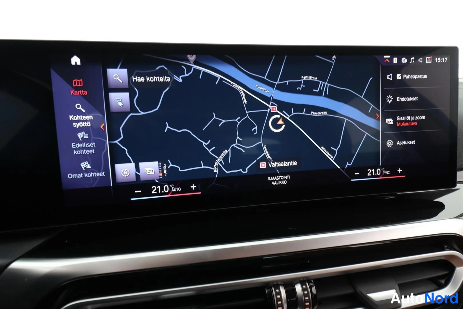Muu: BMW:n infotainment-näyttö näyttää navigointikarttaa, jossa lukee Hae kohteita ja Valtaalantie, sekä ilmastoinnin lämpötilaa 21,0 astetta.