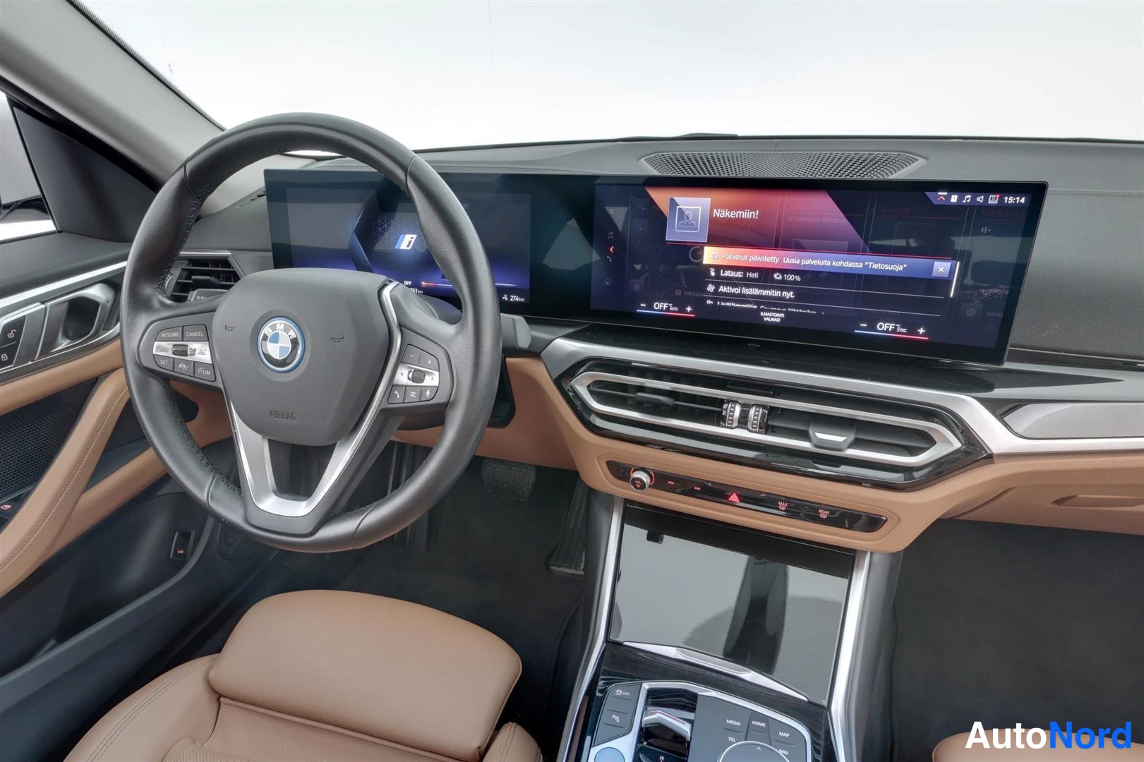 Muu: Lähikuva ohjaamosta: BMW-ohjauspyörä ja kaareva näyttö, jolla suomenkielinen teksti 'Näkemiin!' ja lataustiedot 'Lataus: Heti 100%'. Ruskea kojelauta ja ilmasto