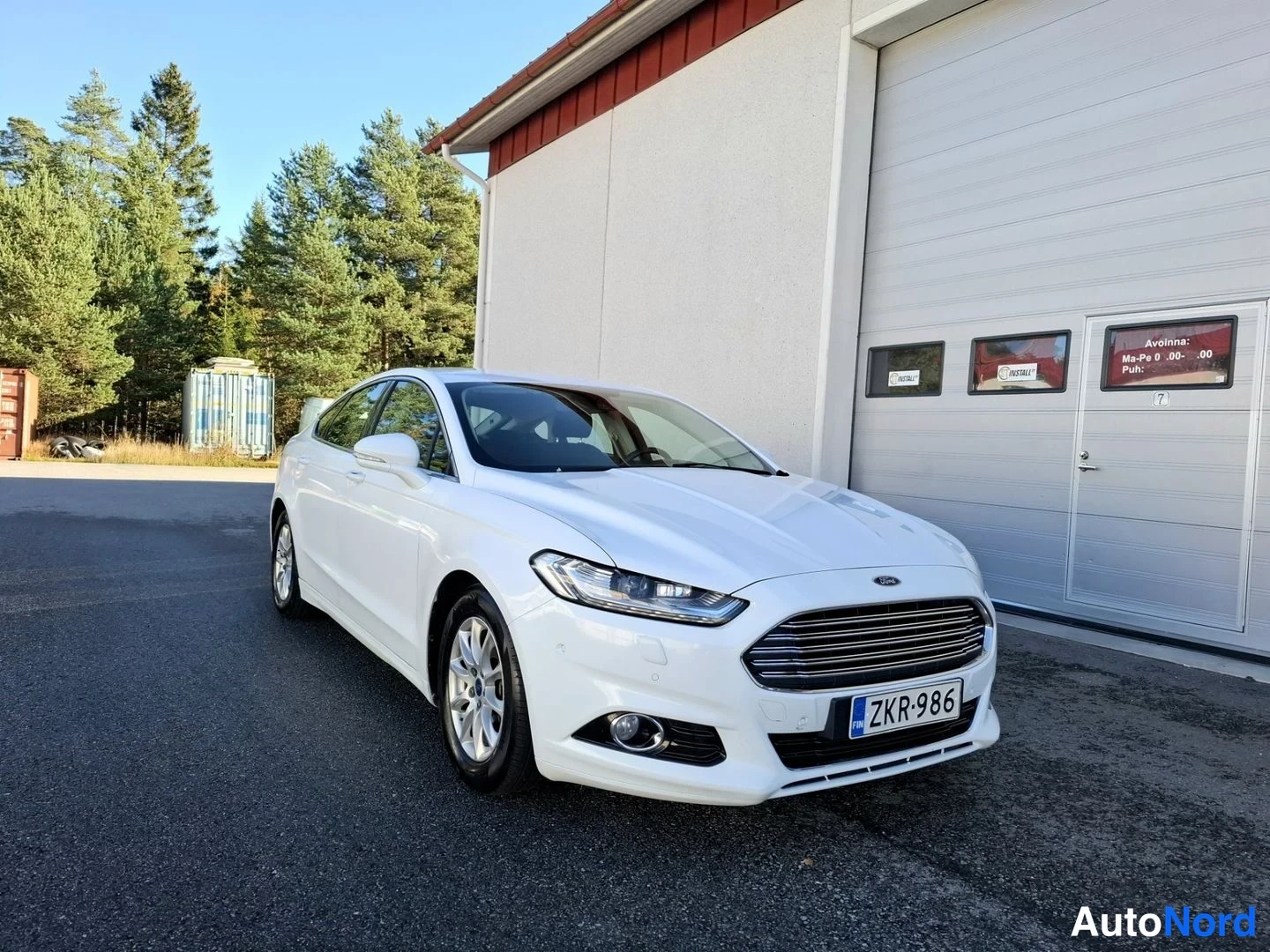 Etuviisto, nokka oikealle: Valkoinen Ford Mondeo etukulmasta oikealta, etusäleikö ja rekisterikilpi näkyvissä.