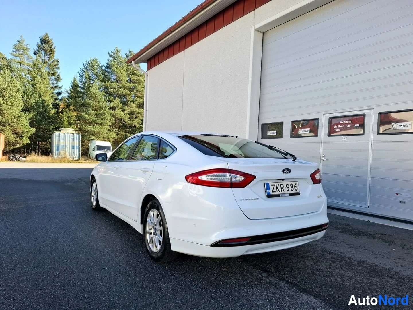 Takaviisto: Valkoinen Ford Mondeo takakulmasta, takavalojen, Ford-merkin ja rekisterikilven näkyessä.
