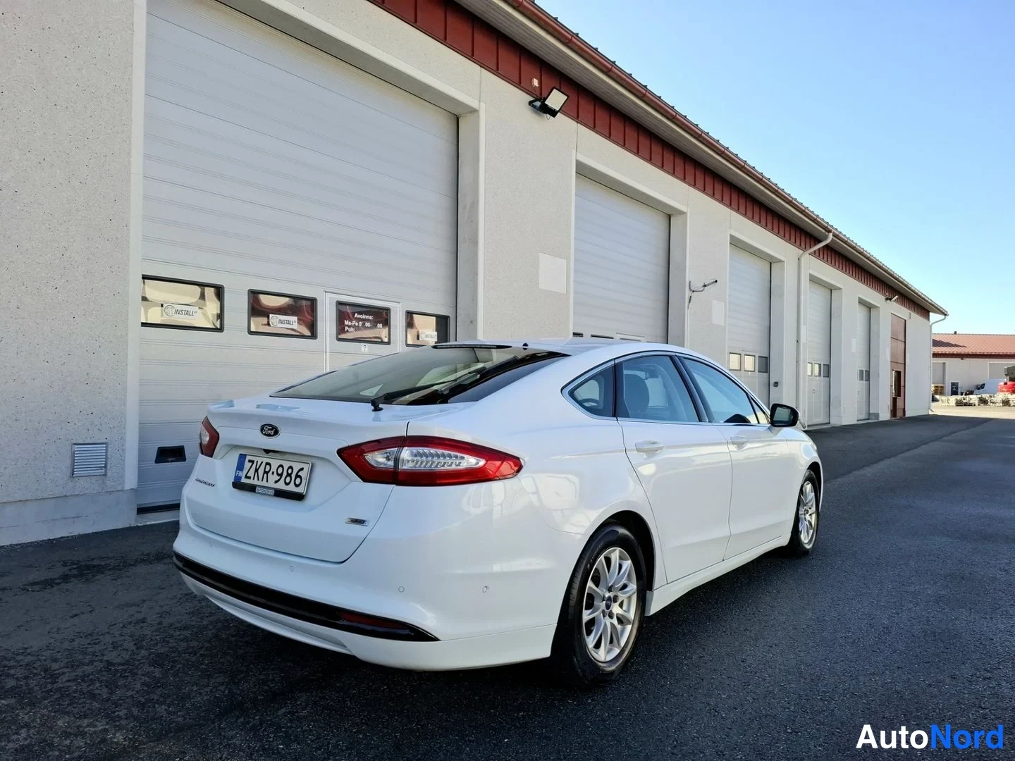 Takaviisto: Valkoinen Ford Mondeo takakulmasta vasemmalta, takavalojen ja rekisterikilven näkyessä.