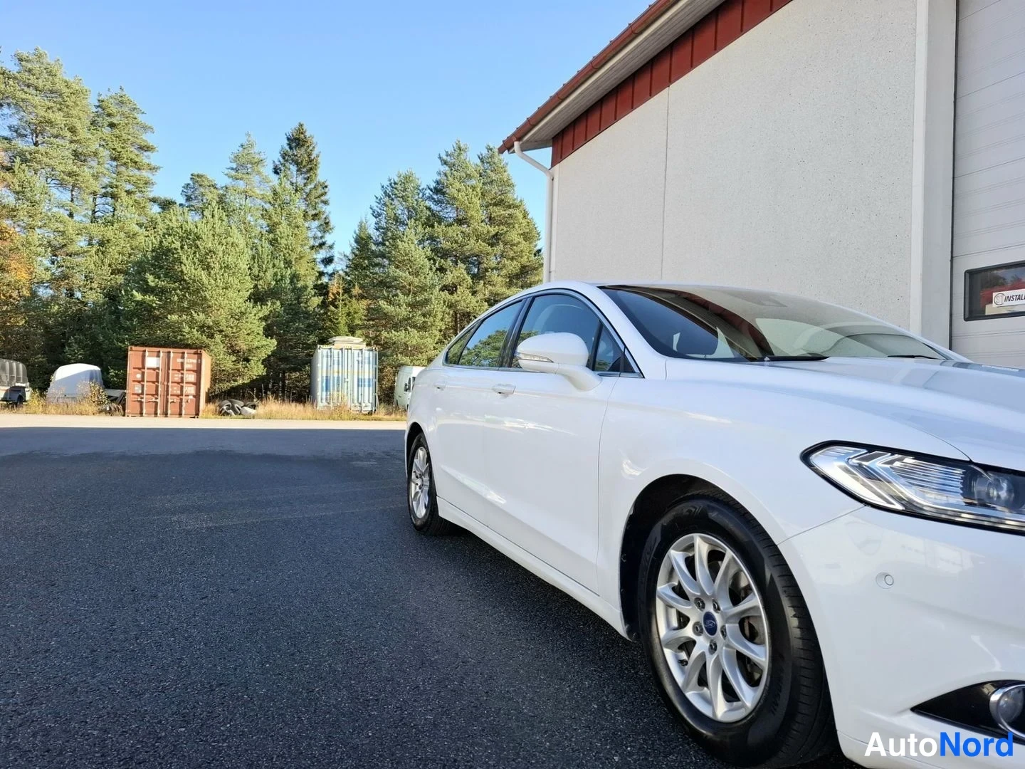 Etuviisto, nokka oikealle: Valkoinen Ford Mondeo -sedan kolmannesviistosta keulasta oikealle, etupyörä ja kylki näkyvissä.