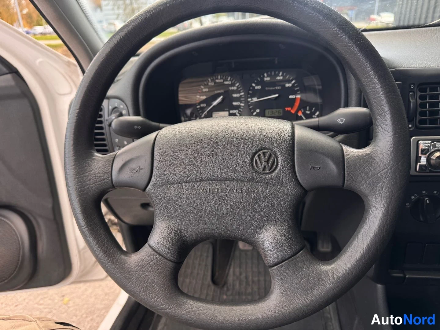 Muu: Ohjaamon näkymä Volkswagen-vaihtelevan ohjauspyörän ympärillä; ilmatyynymerkinta AIRBAG, mittaristo ja radiot中panelin reuna näkyvät.