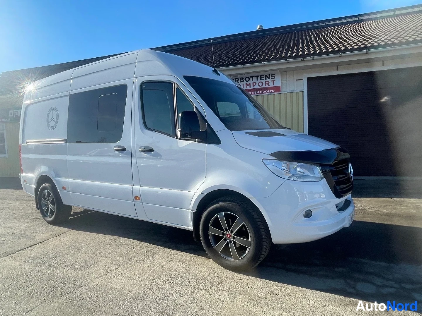 Etuviisto, nokka oikealle: Valkoinen Mercedes-Benz Sprinter etukulmasta, keula ja sivu näkyvät talvella auringonpaisteessa