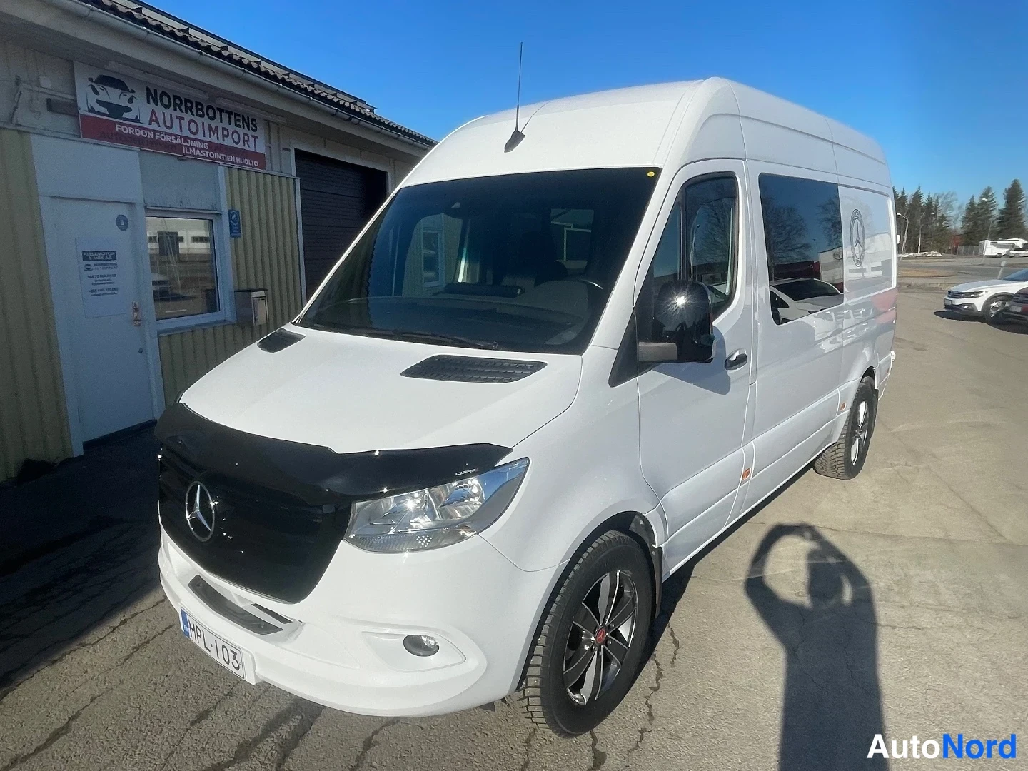 Etuviisto, nokka vasemmalle: Valkoinen Mercedes-Benz Sprinter -pakettiauto etukulmasta, keula vasemmalla, tumma etuspoileri ja mustat kevytmetallivanteet.