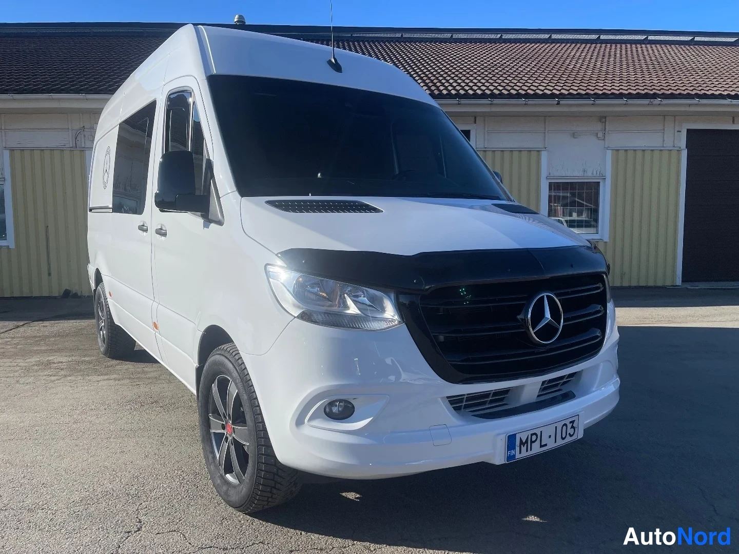 Etuviisto, nokka oikealle: Valkoinen Mercedes-Benz Sprinter -pakettiauto etukulmasta, keula oikealla, musta etuspoileri ja rekisteritunnus.