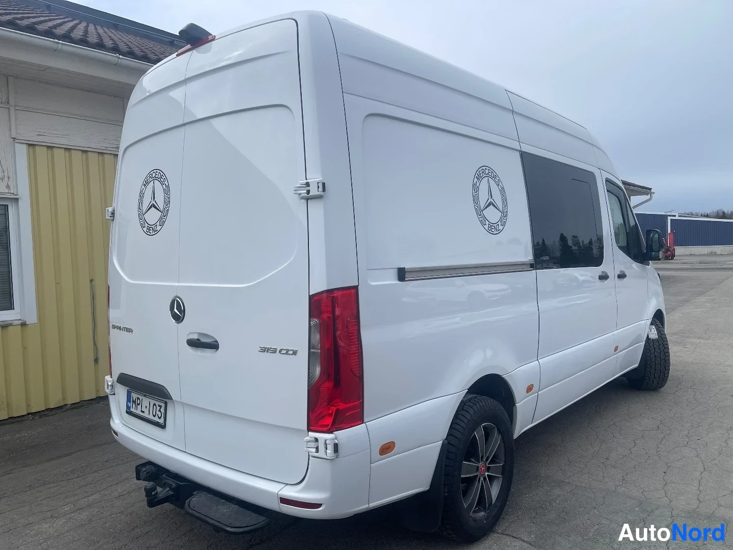 Takaviisto: Valkoinen Mercedes-Benz Sprinter takaosan kolmasosasta oikealta, kylkikelkalla kiinteä kisko ja tunnus 319 CDI.