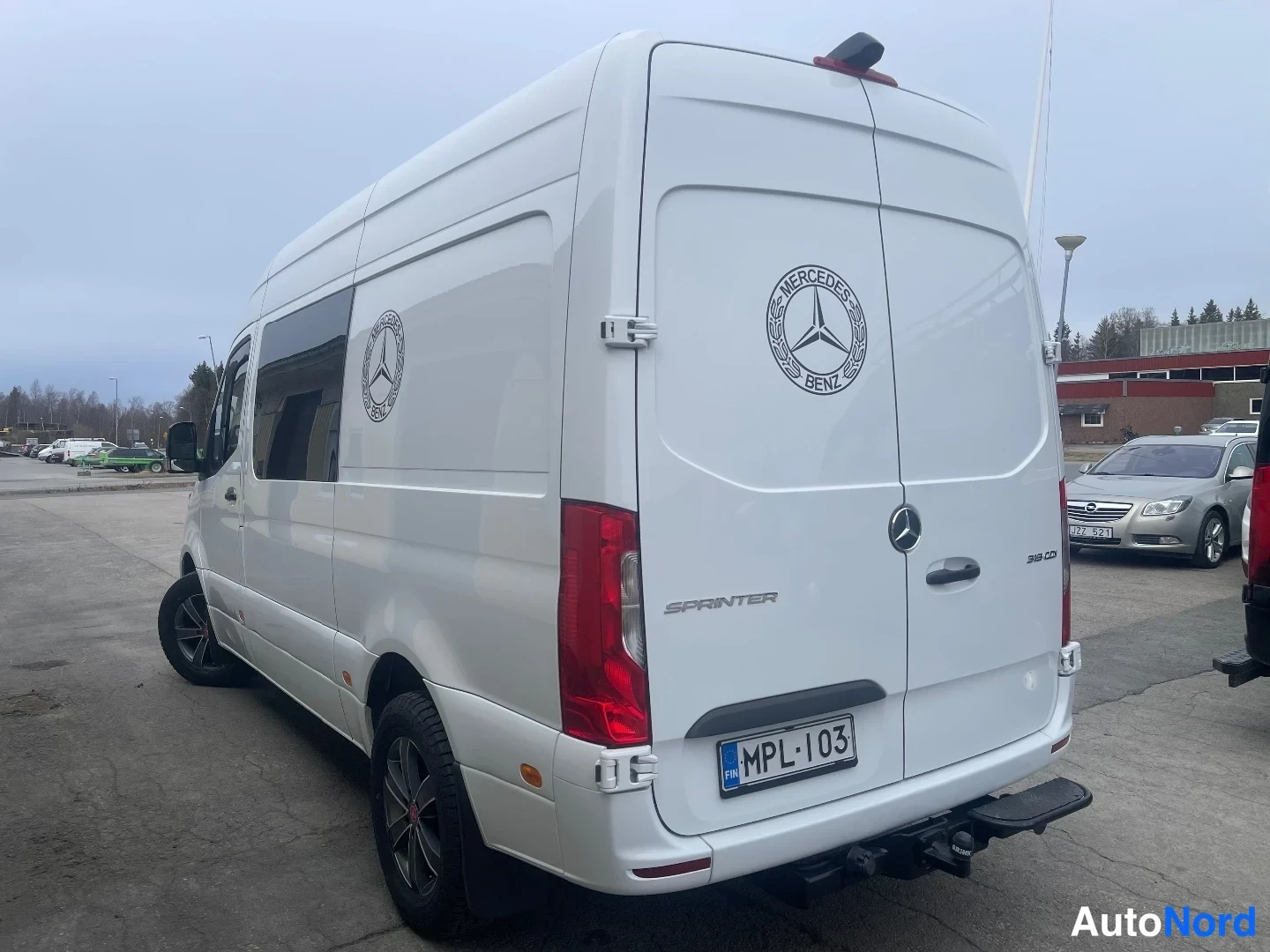 Takaviisto: Mercedes-Benz Sprinter -pakettiauto takaa viistosti oikealta, valkoinen koritakki, rekisterikilpi ja takavaijerikytkin.