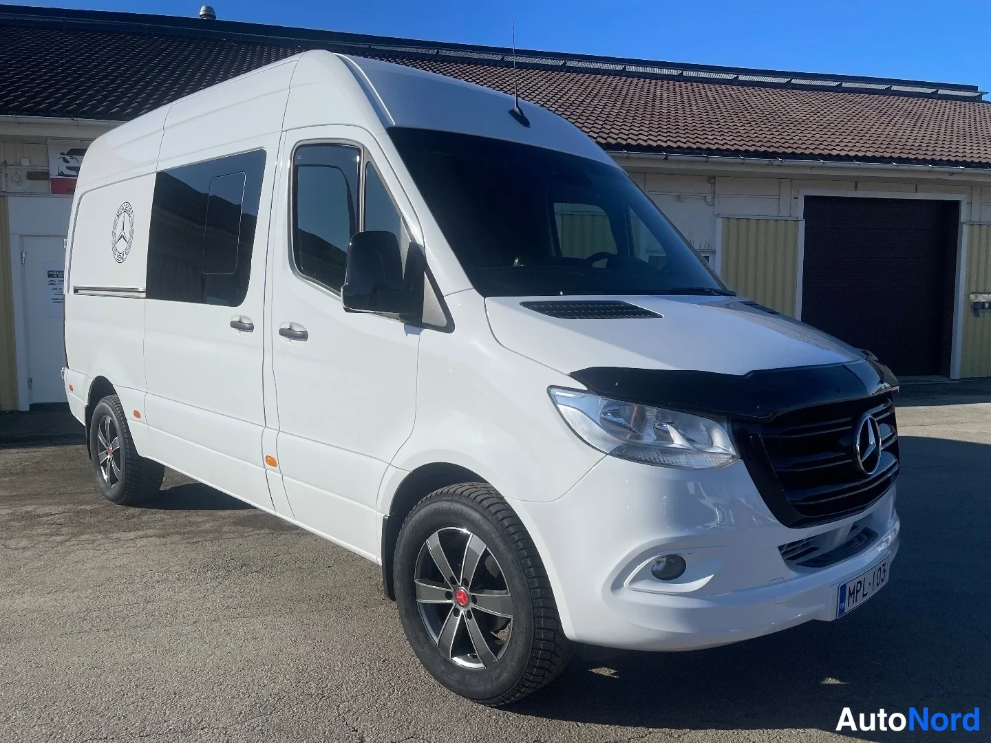 Etuviisto, nokka oikealle: Valkoinen Mercedes-Benz Sprinter -pakettiauto kolmannelne asema oikealta edestä, rekisterikilpi näkyvissä.