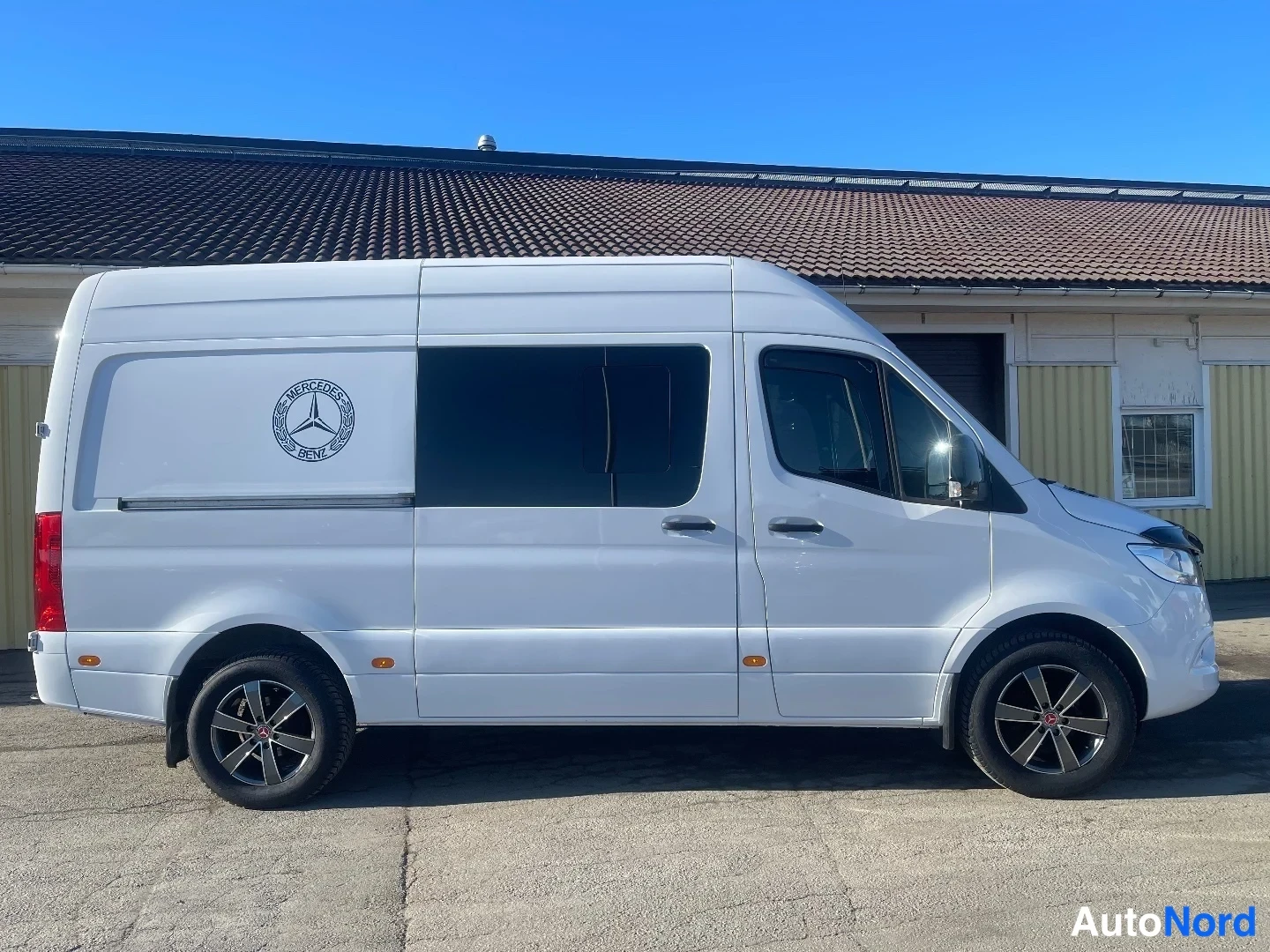 Takaviisto: Valkoinen Mercedes-Benz Sprinter -pakettiauto kolmannelne asema takaa vasemmalta, kyljessä Mercedes-Benz-merkki.