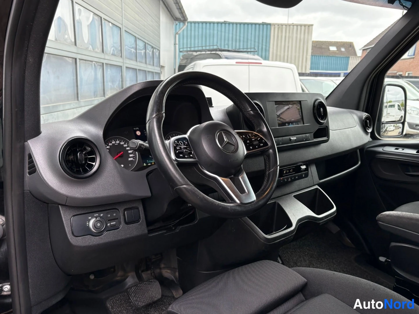 Muu: Mercedes-Benz pakettiauton kuljettajan puolen cockpit: ohjauspyörä tuntomerkkeineen, analogiset mittarit, keskikonsoolin infotainmentnäyttö ja kangasistuin.