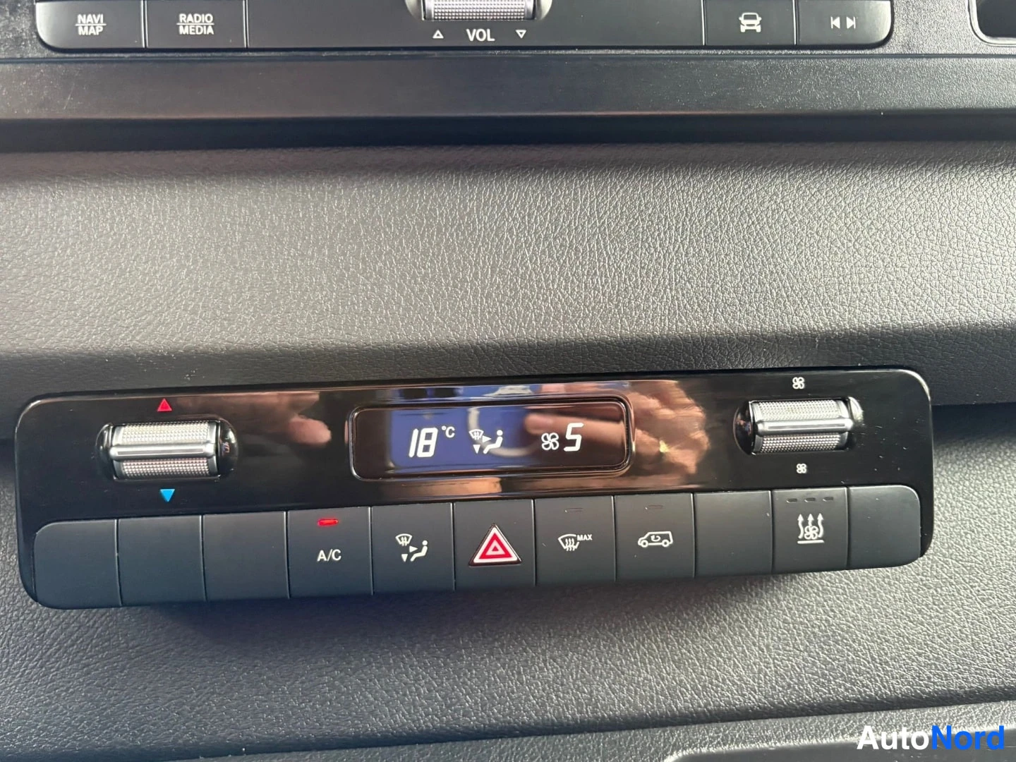Muu: Keskikonsolin automaattinen ilmastointipaneeli, jonka näytössä lukee 18 °C ja puhallustaso 5; näkyvät A/C-painike, varoitusvalo ja takalasin lämmityspainike.