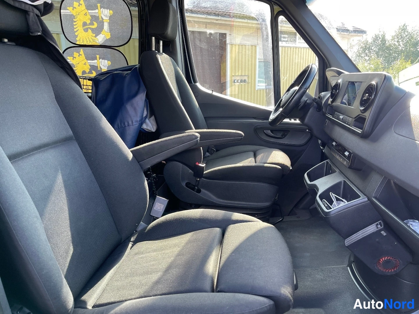 Muu: Ohjaamosta kaksi tummaa kangasistuinta kuljettajan istuimen käsinojalla, mittaristö ja Android Auto -käyttöliittymä näkyvät oikealla.