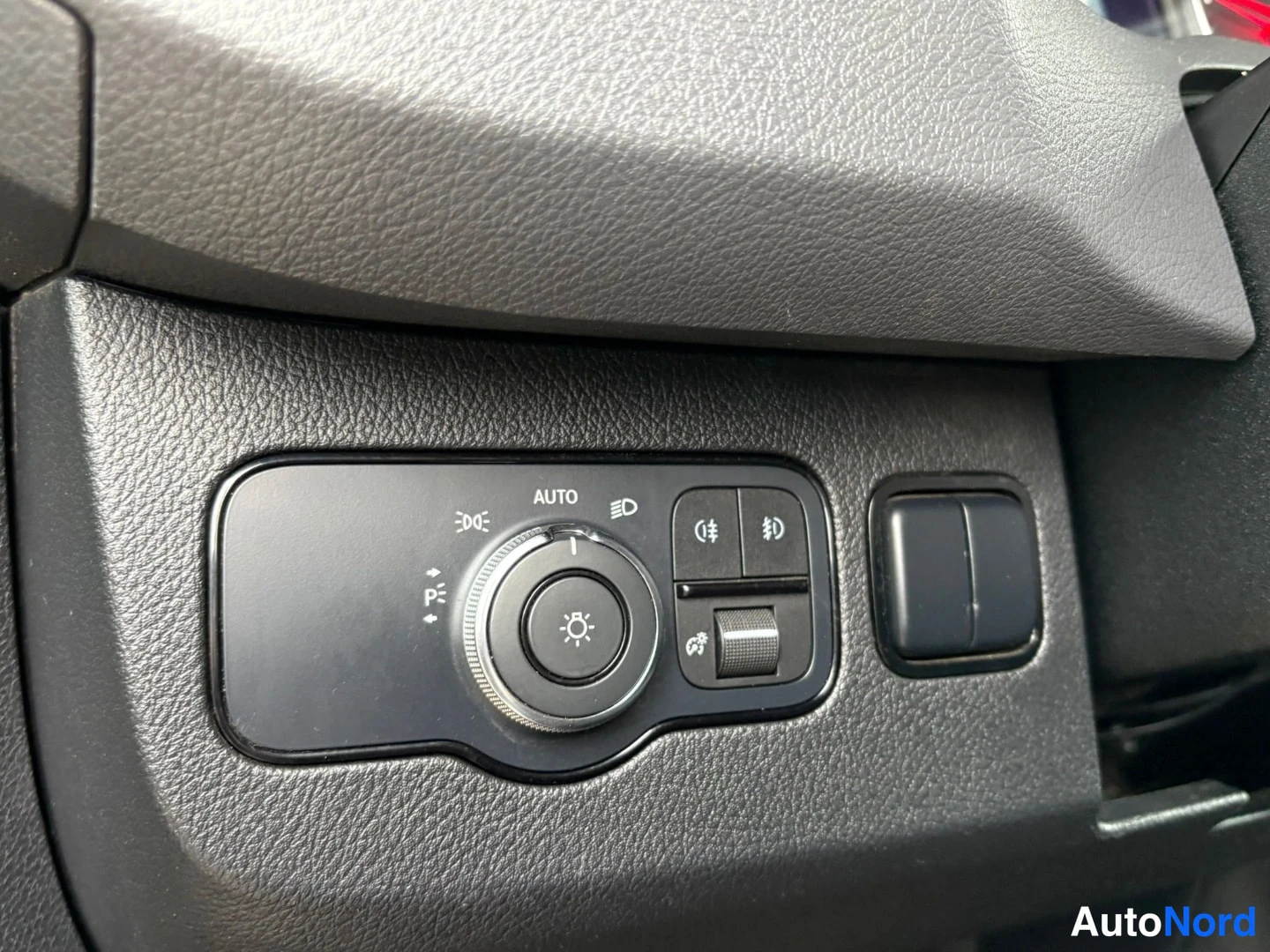 Muu: Tarkempi kuva kojelaudan valokytkimestä, jossa on AUTO-merkki ja sumuvalojen kytkin.